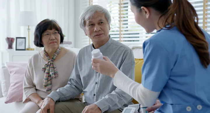 Young caregiver in scrubs uniform showing medicine to Asian family