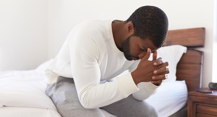 Depressed man looking unhappy sitting on side of the bed